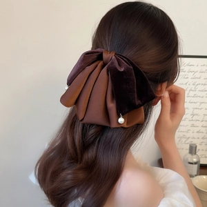 Detail of dark brown velvet bow hair clip with elegant pearl pendants on model hairstyle