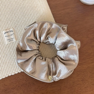Gros plan détaillé d'un chouchou en satin champagne avec un pendentif logo doré poli