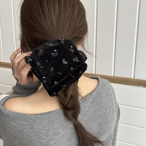 Elegant black velvet scrunchie with blue floral pattern worn on a low ponytail hair style