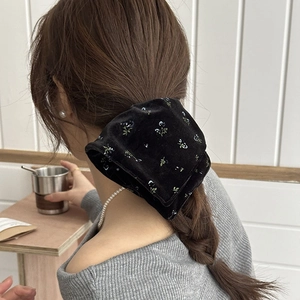 Detail of black velvet scrunchie with blue and white floral embroidery on a soft fabric texture