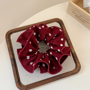 Detail of burgundy polka dot scrunchie with ruffled edges in a wooden display tray