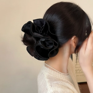 Close-up of a large black satin scrunchie with elegant layered pleats in a ponytail