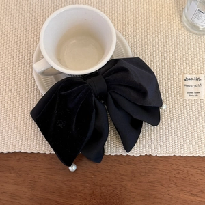 Detail view of a black velvet ribbon hair claw clip with pearl accents on a white cup