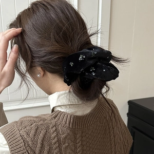 Detailed close-up of a black velvet scrunchie with white floral patterns on a ponytail
