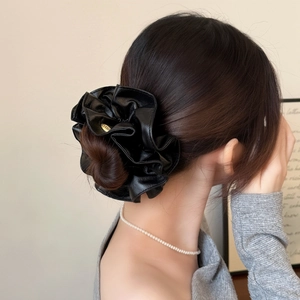 Close-up of black leather scrunchie with gold metal logo on elegant low bun hairstyle