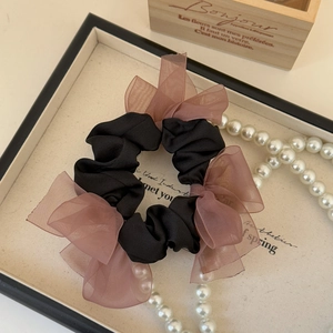 Detail of elegant black satin scrunchie with three pink organza bows on a display tray