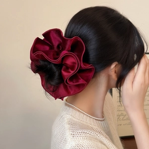 Detailed view of a dark red velvet scrunchie showing ruffled texture on a bun hairstyle
