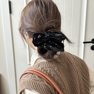 Close-up of a black velvet scrunchie with floral embroidery on a ponytail