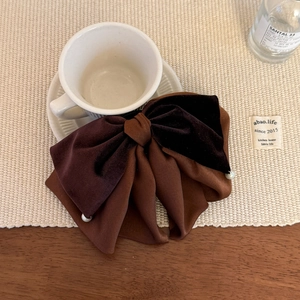 Detail of luxury velvet and satin bow hair clip with pearl accents on a white mat