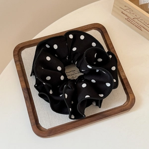 Close-up of a black and white polka dot scrunchie on a wooden tray for elegant hair styling
