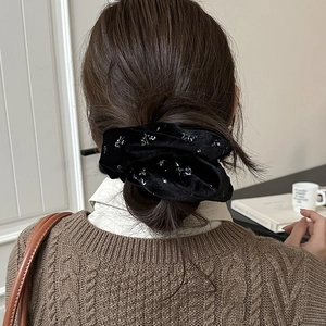 Detail of a black velvet floral scrunchie worn on a brown ponytail for an elegant look
