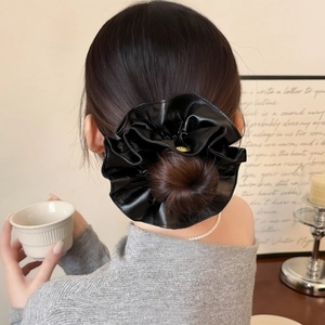 Large black faux leather scrunchie with gold LE logo charm on model bun