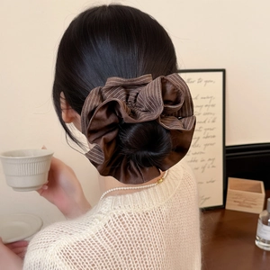 Close-up of a striped brown satin scrunchie styling a bun on a model's head