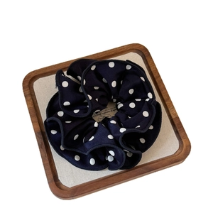 Double-layered black polka dot scrunchie on a wooden tray for elegant hairstyles