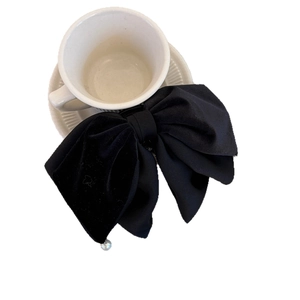 Elegant large black velvet bow hair clip with pearl pendant detail on ceramic cup