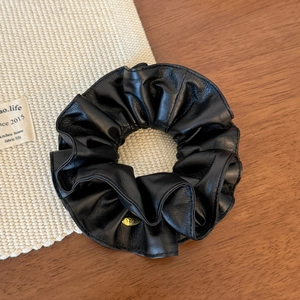Close-up of black leather scrunchie with pleated texture and gold metal tag detail