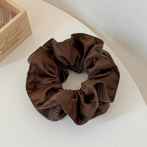 Detailed close-up of brown striped silk scrunchie with soft fabric folds on white surface