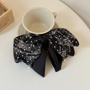 Detail of a large bow hair clip with black polka dots, plaid fabric and pearl pendants