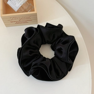 Detailed view of a large black velvet scrunchie with soft pleats on a white surface