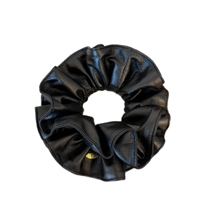 Elegant black faux leather scrunchie with pleated texture and round gold metal label