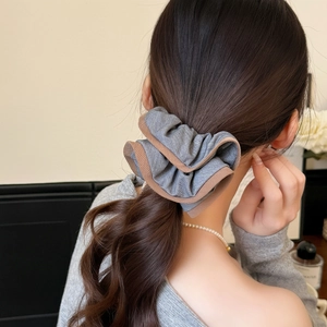 Détail d'un chouchou gris plissé avec bordure marron sur une coiffure queue de cheval
