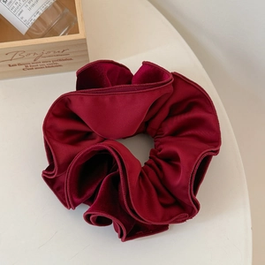 Detailed macro view of a large burgundy velvet scrunchie with elegant pleated texture