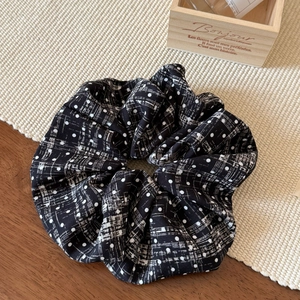 Close-up of black velvet scrunchie with white polka dots and grid patterns on a woven mat