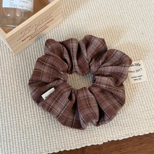 Detailed view of a brown plaid scrunchie on a woven mat with vintage wooden props