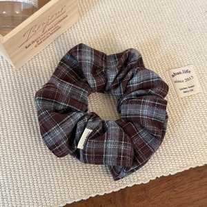 Detailed view of checkered brown hair scrunchie with a Hand Made label on fabric