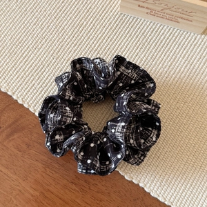 Detail of black velvet scrunchie with white checkered dots on textured beige mat