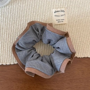 Détail d'un chouchou en tissu gris avec bords marron sur un fond de table texturé