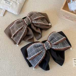 Elegant plaid bow hair clips with plush edges and pearl accents on a beige woven mat