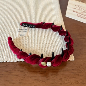 Macro detail of burgundy velvet twisted headband with pearl accent and gold metal emblem
