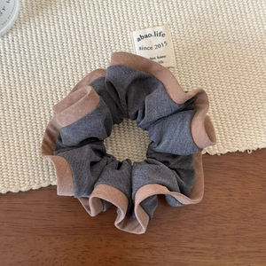 Détail d'un chouchou gris plissé avec liseré marron café sur un support tressé chic