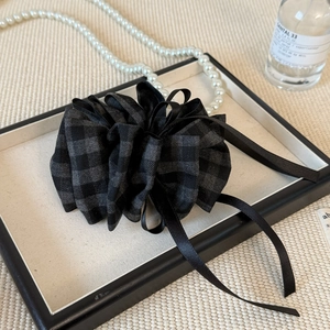 Close-up of a plaid fabric flower hair claw clip with black satin ribbons on a tray