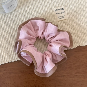 Détail d'un chouchou rose plissé avec bords côtelés marron sur fond chaleureux