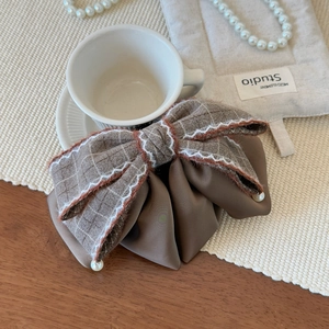 Detail of tweed and satin bow hair clip with pearl accent on a wooden table