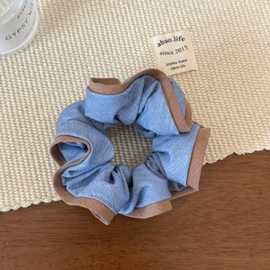 Vue détaillée d'un chouchou en denim bleu avec finition de bordure en ruban marron