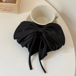 Detail of a black satin ribbon hair claw clip with long streamers on a white table