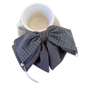Dark grey plaid bow hair claw clip with elegant pearl pendants on a white coffee cup