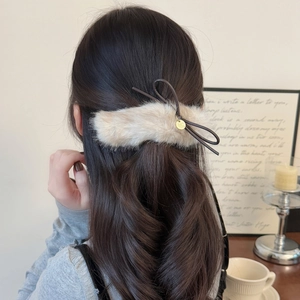 Detail view of a plush beige bow hair clip styled in a cozy indoor setting