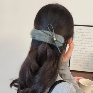 Detail view of a gray plush bow hair clip with golden charm on long wavy hair