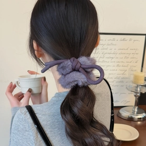 Chouchou en peluche violet foncé avec nœud porté sur une coiffure en queue de cheval