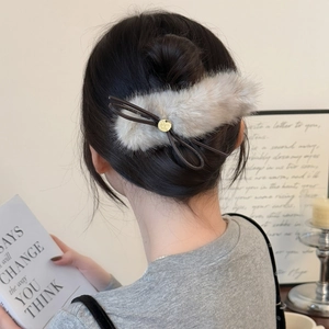 Detail of plush grey bow hair clip with gold metal emblem on casual bun hairstyle