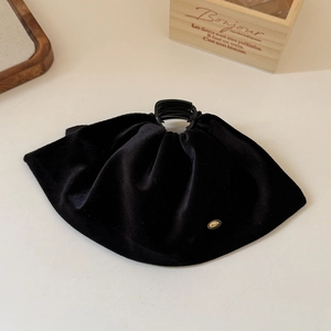 Detailed view of large black velvet hair claw with soft pleats and gold metal logo
