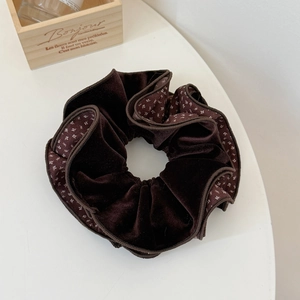Detailed view of large dark brown velvet scrunchie with floral edge on a white surface