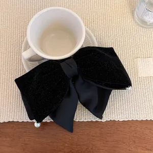 Detail of black velvet and satin bow hair clip with faux pearls on beige woven mat
