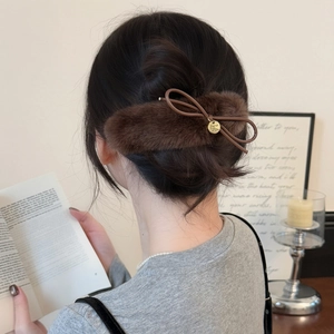 Detail of plush brown bow hair clip with gold logo pendant on low bun hairstyle