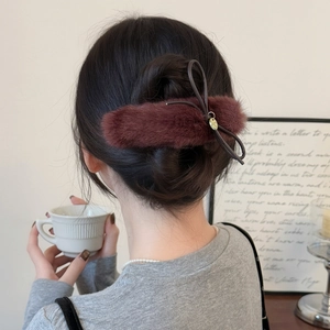 Detail of plush wine red bow hair clip with gold metal pendant on a hair bun