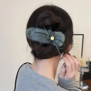 Close-up of grey plush faux fur bow hair clip with gold metal tag on black hair